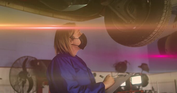 Automotive technician pausing notes then inspecting raised tire, animated overlay measuring tread