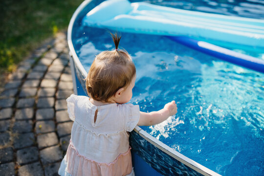 Little girl splashing water in backyard pool during summer day.