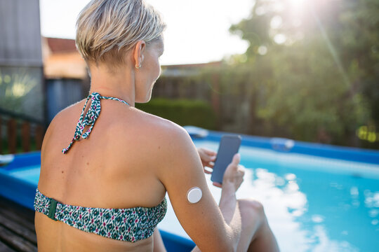 Woman using smartphone with wearable health sensor on arm.