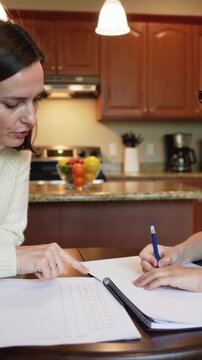 Vertical video: Pointing mom cream-knit guiding child writing sheet with blue pen at home homework