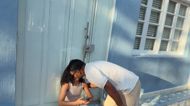 Young man approaching and kissing his girlfriend sitting in a colorful colonial street on vacation