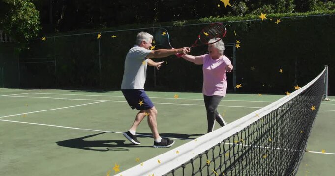 Senior couple moving to volley on sports court hitting rackets bumping hugging yellow stars overlay