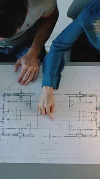 Vertical video: Starting placing hands, right man pointing axis on blueprint table in grey and teal