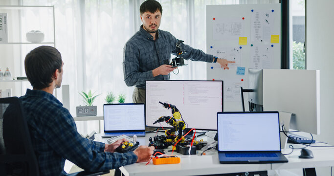 Team adult male engineer develop present AI robotics hand project at tech workspace. Artificial intelligence, collaboration support prototype development, robotic, debugging, machine learn, training.