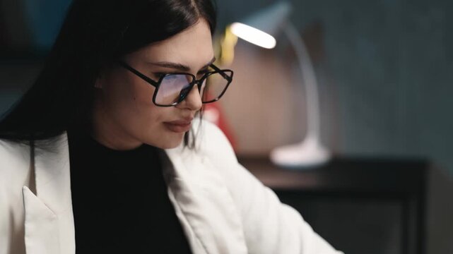 Close-up of professional businesswoman in glasses working on computer in office late evening. Business work concept.

