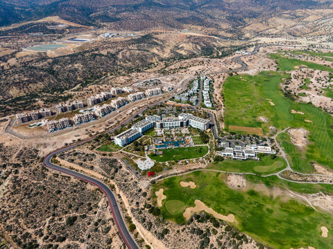 Aerial drone view of the beautiful Taghazout Bay coastline featuring luxury resorts, sandy beaches, lush green golf courses, and the Atlantic Ocean in Agadir, Morocco.