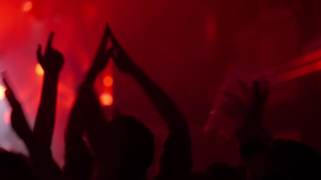 Dynamic video showing a silhouetted crowd raising hands and applauding at a vibrant live music concert or club party. Energetic atmosphere with flashing red stage lights creating a captivating visual