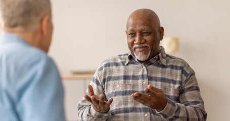 Two men have a conversation in a community center. One man is smiling and using hand gestures while...