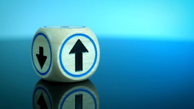 A white die with up and down arrows on adjacent sides on a blue gradient reflective surface from a close-up viewpoint.