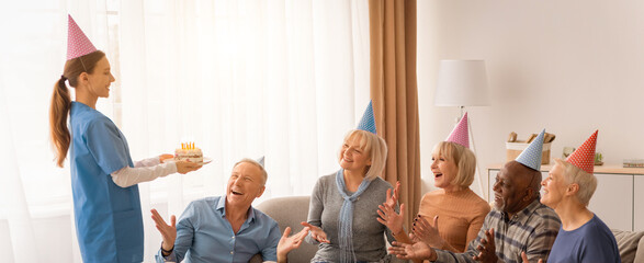 Obraz premium A group of seniors gather in a living room to celebrate a birthday. One person brings a cake while others smile and enjoy the moment. Everyone wears party hats and shares laughter.