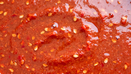 Macro background of spicy red chili pepper paste with oil and visible seeds top view