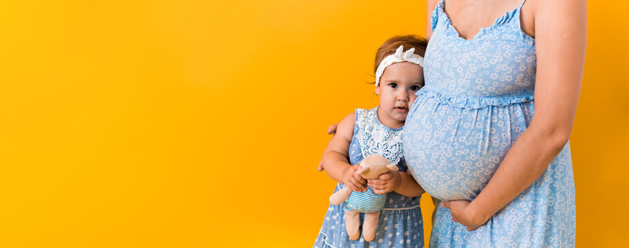 Motherhood, femininity, hot summer - croped banner pregnant unrecognizable woman mother in blue dress little happy girl baby sibling with teddy bear hugs care mom's big belly on yellow background