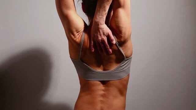 Sport body woman doing stretching exercises for shoulders, scapula, healthy back from pain after fitness train Slim naked muscles model in bra isolated in studio light with copy space. Back view