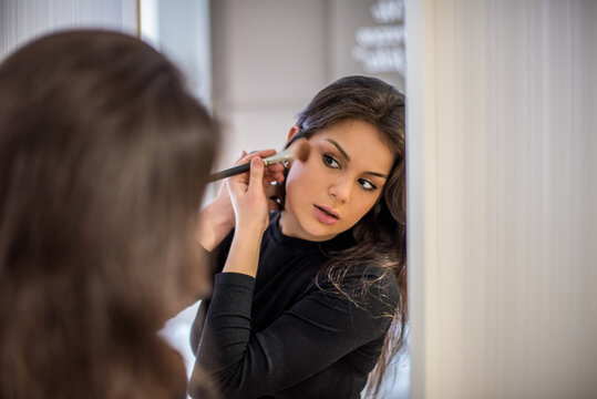 Woman applying makeup with a brush in the mirror