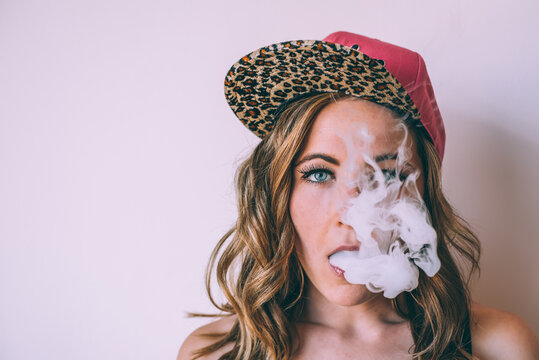Young woman exhaling smoke while wearing a leopard cap