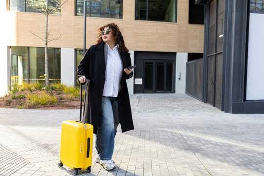 Confident businesswoman traveling with yellow suitcase