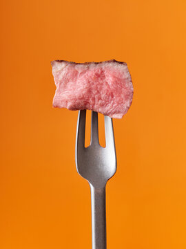 Juicy steak on fork against vibrant orange background