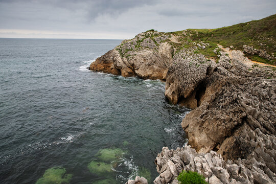 Rocky cliff with natural cave and the Atlantic Ocean under a cloudy sky