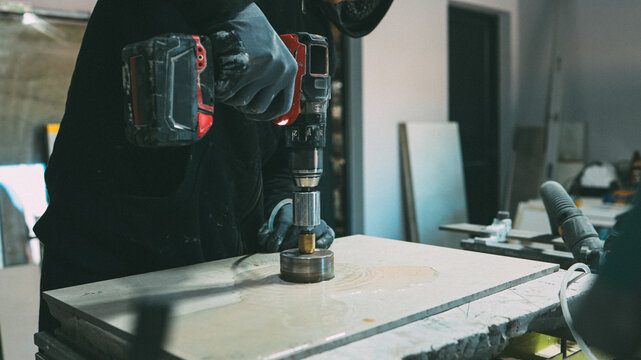 Craftsman using a diamond core drill bit to cut a precise hole in a stone slab