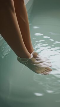 Vertical video: Lowering bare legs and feet into tub water, creating circular pale green ripples