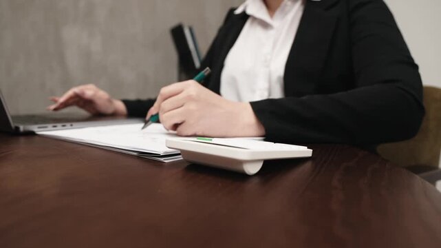 Close-up of female office professional using calculator for calculations at workplace. Finance and accounting concept.
