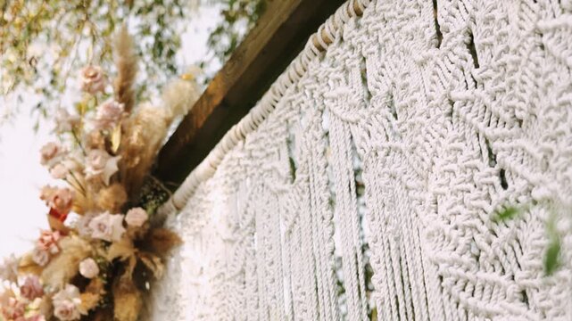 Macrame backdrop with dried floral arrangement, soft neutral palette, intricate knotwork and cascading fringe