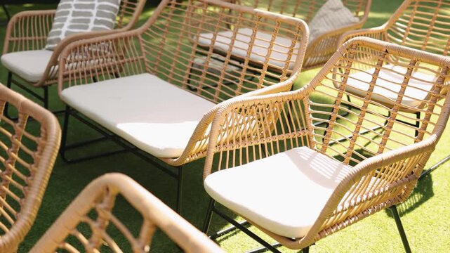Sunlit rattan chairs arranged outdoors, wedding decor with cushion seats, wicker benches and patterned pillows