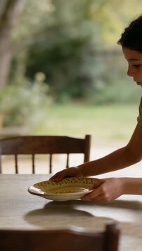 Vertical video: Entering from right, child placing plate on porch table for meal, copy space