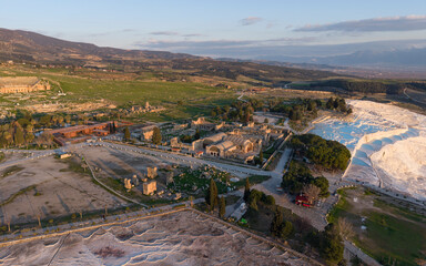 Aerial drone view of Hierapolis Antik Kenti and the famous Pamukkale travertines in Denizli, Turkey, showing ancient ruins, Roman theater, columns, and scenic landscape from above.