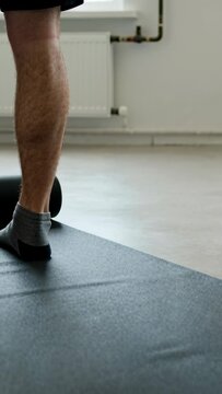 Vertical video: Placing foot, man feet in gray socks shifting on mat at home, preparing for roller