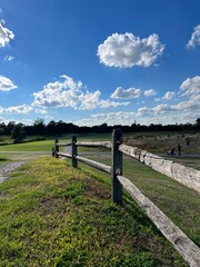 Fototapeta premium Fence leading to an open fairway on a golf course with blue sky and white clouds