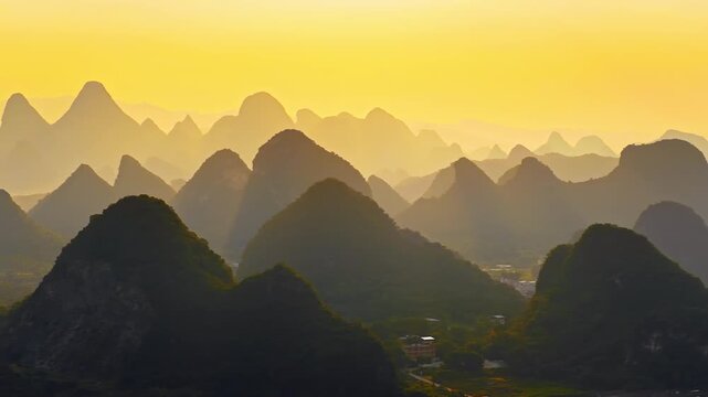 Panoramic view of karst limestone mountains in Guilin, China, during golden sunrise with misty atmosphere.