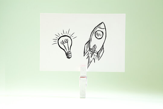 Drawing of rocket and light bulb on white paper. Startup concept