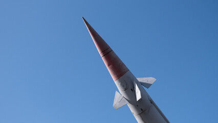 Rocket Nosecone Pointed Toward Sky, Sharp Red Tip Against Clear Blue Backdrop, Smooth Aerodynamic Panels And Rivets Visible, Telemetry Instrumentation Implied, Test Range Atmosphere