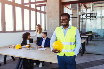 Smiling Construction Engineer in High-Vis Vest Holding Hard Hat in Modern Office Meeting