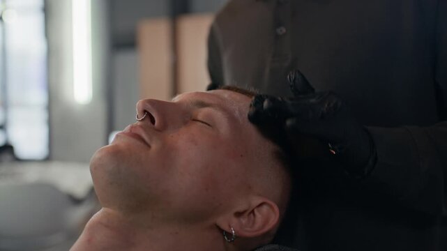 Close up of anonymous barber using facial cream while massaging face of client who enjoying process