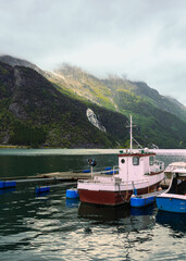 Fototapeta premium Tyssedal fjord atmosphere as small fishing boat anchored by floating dock on calm fjord water with steep mountains and waterfall behind, regional coastal scenery and tourism promotion