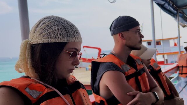 Group of young tourists bored in boat wearing orange life vests before sea trip starts.