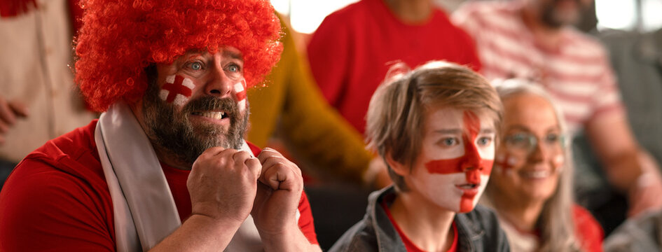 Excited football fans supproting English national team in live soccer match at stadium.