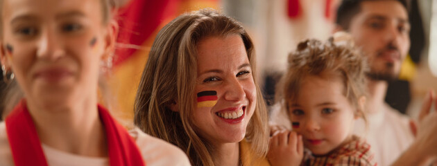 Fototapeta premium Excited football fans, mother with little daughter, supproting German national team in live soccer match at stadium.
