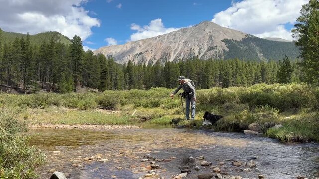 Woman fly fishing with her Sheltie dog in Colorado's high country. This is on Red Mountain Creek in Taylor Park.