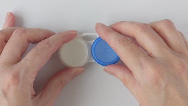 Hands tighten the lid of a contact lens case. Concept for eye care and lens hygiene. White container with compartments for safe contact lens storage.