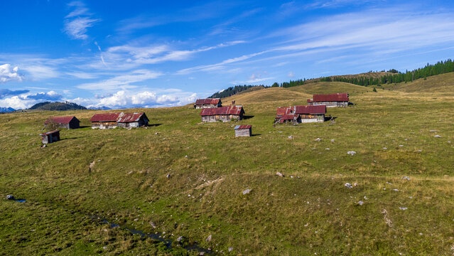 Aerial photograph of the Marcesina Plateau in the Italian Prealps, featuring traditional "Casoni". Historic, rustic mountain cabins with distinctive rusty red corrugated roofs