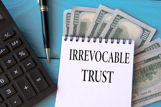 IRREVOCABLE TRUST - words in a notebook on a blue background with banknotes, a calculator and a pen