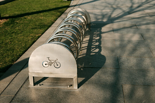Metal bicycle parking rack casting long shadows on the pavement. Urban cycling infrastructure along the riverside walkway in Belgrade.