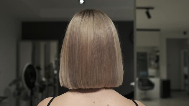 Back view of a woman with a perfectly straight blonde bob haircut in a professional beauty salon