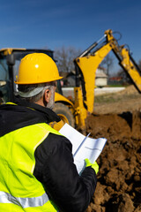 Engineer inspecting excavation work and documents near heavy machinery