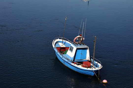 Blue fishing boat anchored in calm waters with ample negative space