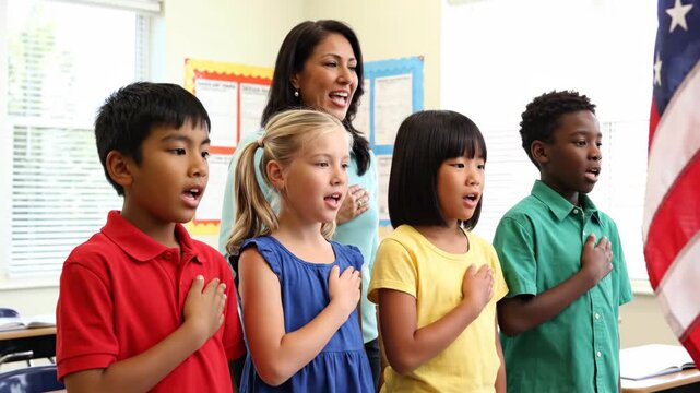 Teacher and primary school student standing in classroom pledging allegiance to flag. Group of diverse child with woman reciting patriot pledge for national day.