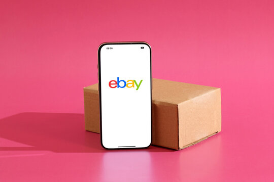 EBay logo displaying on smartphone screen with cardboard box against pink background, representing online shopping and delivery